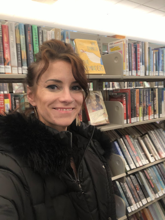 Photo of the author standing in front of a stack of books at a library.